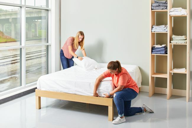 две жени оправят легло с бели чаршафи